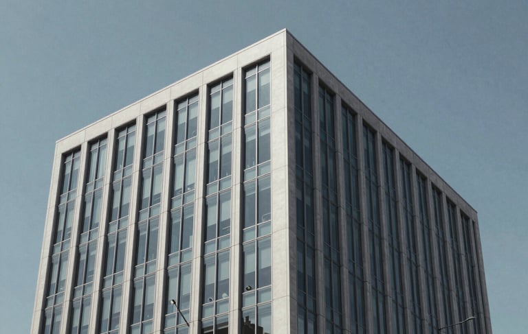 A sharp, professional photography shot of a modern North American office building exterior with clean glass lines and a light gray facade, set against a clear blue-gray sky. Minimalist architectural style reflecting business sophistication.