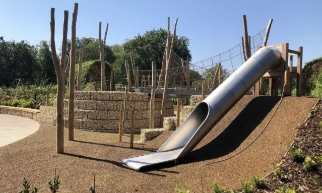 Playground moderno com escorregas, cordas para escalar, balanços e áreas separadas por faixa etária.