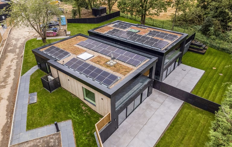 Aerial view of modern eco-friendly homes with solar panels and green roofs on a lush landscape.