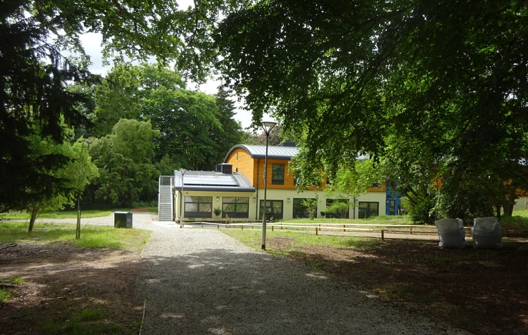 Modern school building viewed through the canopy of trees along a gravel path.