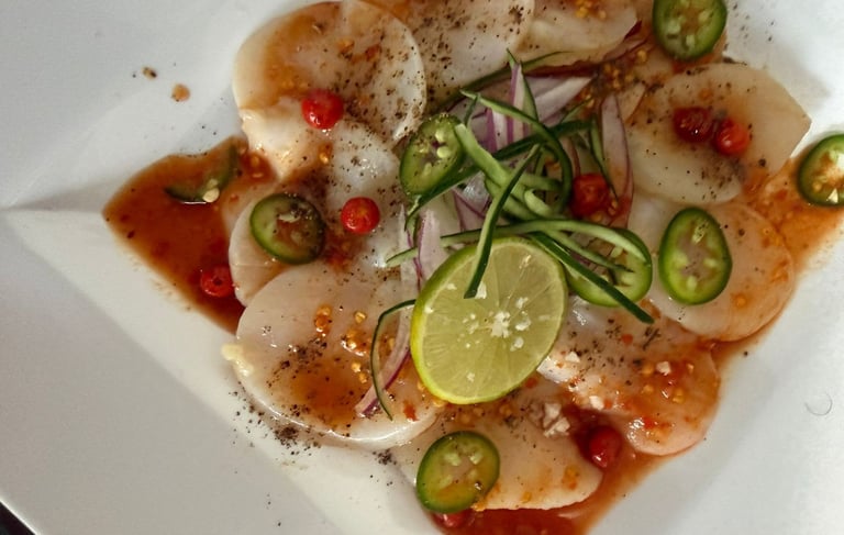 Aperitivo de carpaccio de vieira fresca con lima, rodajas de jalapeño y salsa de chile, servido.