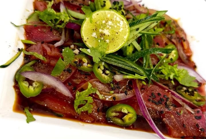 Aguachile de atún fresco con cebolla morada, jalapeños, lima y cilantro en un plato blanco.