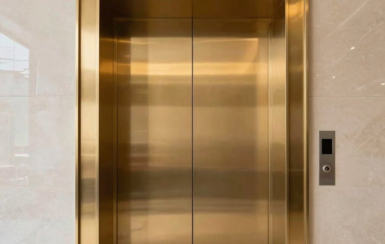 A low-angle, professional architectural photograph of a sleek, modern elevator entrance in a South Asian corporate headquarters. The doors are finished in polished gold, reflecting a minimalist lobby with black marble floors and soft, premium lighting. The composition is centered and symmetrical, projecting corporate reliability and precision.