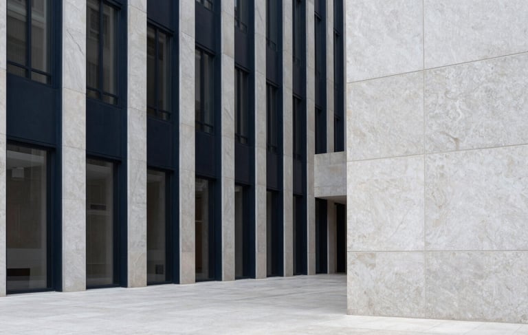 A minimalist architectural photograph of a high-end corporate building lobby in a North American metropolis. The space is defined by strong vertical lines of deep navy steel and expansive panels of light grey stone. The lighting is soft and natural, emphasizing a calm, professional atmosphere. Ultra-clean composition with significant whitespace.