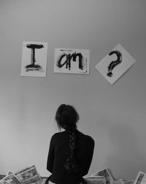 Person standing under “I am?” signs representing self-awareness, identity questioning
