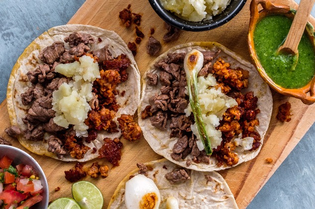 Auténticos tacos callejeros mexicanos con carne de res y chorizo ​​en una tabla de madera con salsa 