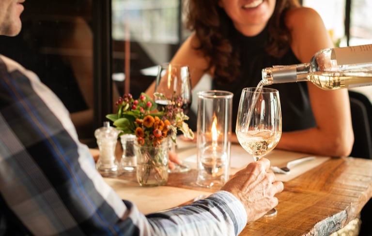 A server pours chilled white wine for a couple during a romantic candlelit dinner date at a rustic restaurant.