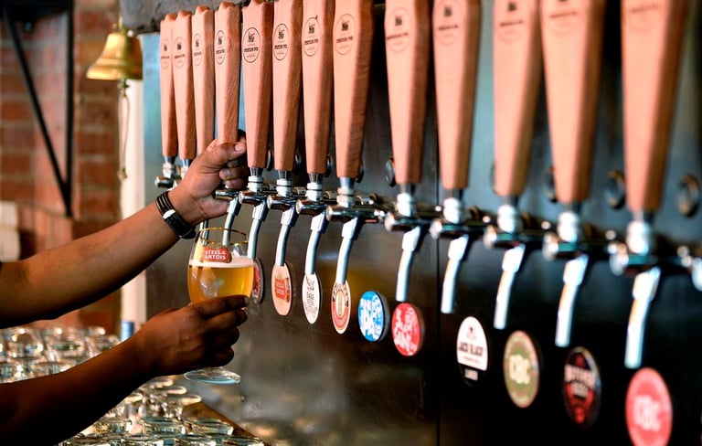 A bartender pours a cold glass of Stella Artois from a row of wooden craft beer taps in a pub.