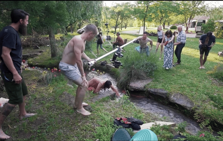 a man is holding a camera rig to film a music video outdoors in the grass