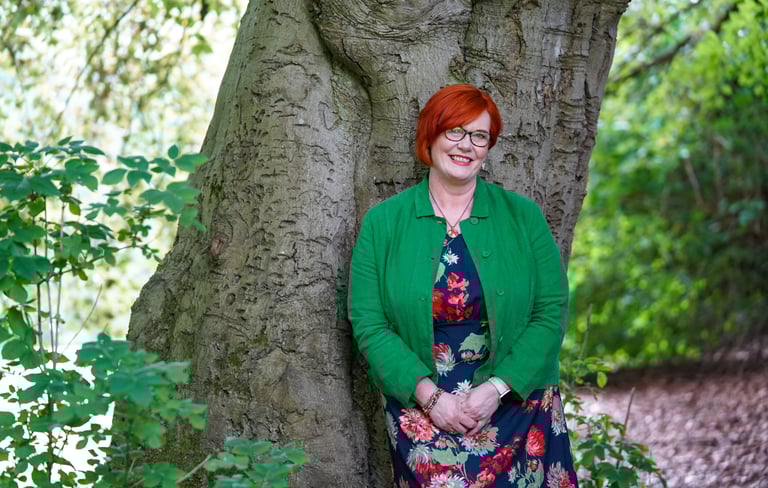 Dawn Vincent Celebrant in a floral dress leaning against at tree