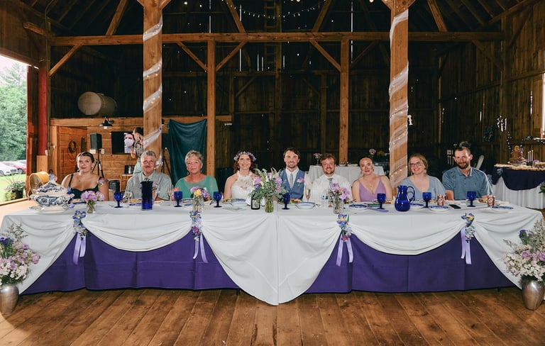 a group of people sitting at a head table with flowers in a wedding reception