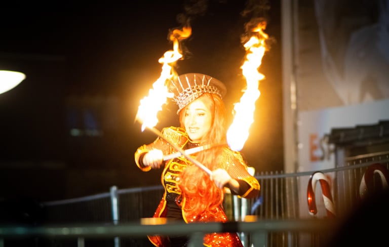 Une femme costumé en train de faire un spectacle avec des bâtons enflammés