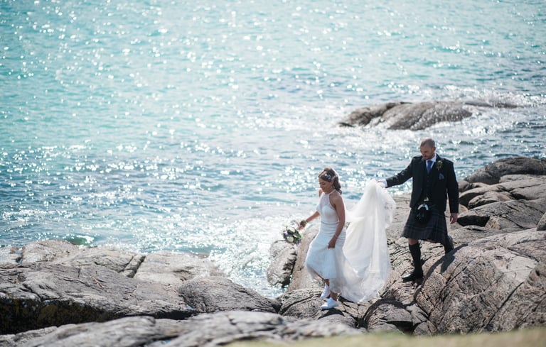 a bride and groom walking down a rocky beach