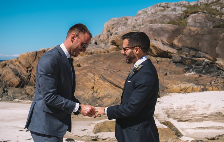 a man in a suit and tie on a beach exchanging rings