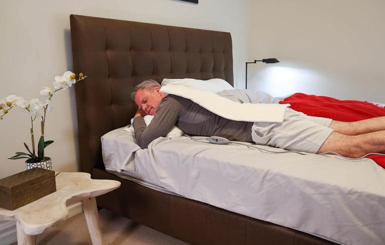Man lying in bed with Thermophore MaxHEAT heating pad on his back for back pain relief