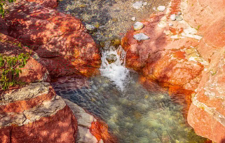 Clear water flowing through red rock formations at Red Rock Canyon in Waterton Lakes National Park.
