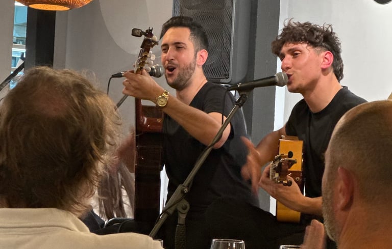 Two male musicians singing and playing SPAN guitars during a live performance at a restaurant venue.