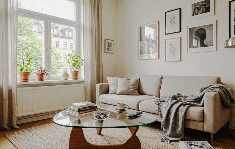  A clean but slightly cluttered living room with a coffee table, mug, books, and a cosy sofa in natural light