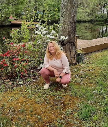 Claudia Smarkola, healer and teacher in a pink sweater and pants casually squatting down