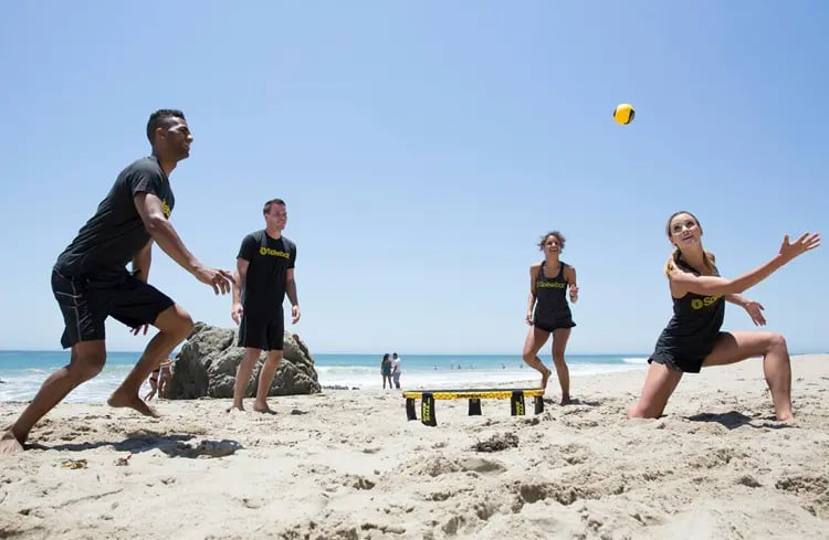 deux équipe de deux personnes s'affrontent au spikeball sur la plage