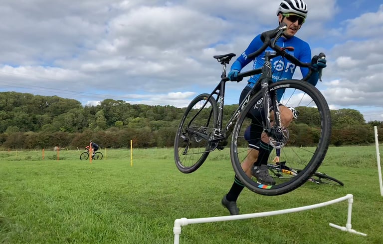 A cyclocross rider carrying their bike over hurdles