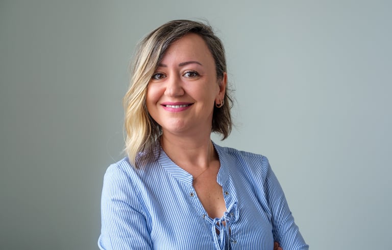 Professional portrait of a smiling woman with blonde highlights wearing a blue striped shirt.