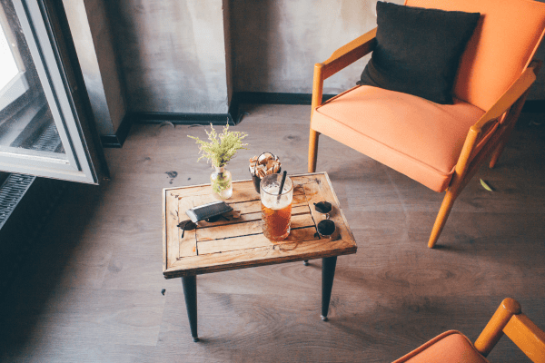 Iced coffee on a rustic wooden table next to a modern orange armchair in a cozy cafe.