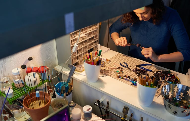 Artesana joyera trabajando con pinzas entre cuentas de colores y materiales de joyería hechos a mano