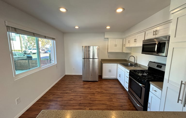 A modern kitchen with white cabinetry, grey countertops, and stainless steel appliances