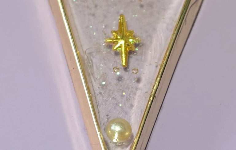 Handmade triangle resin pendant necklace with a gold star, white pearls, and glitter on a black cord.