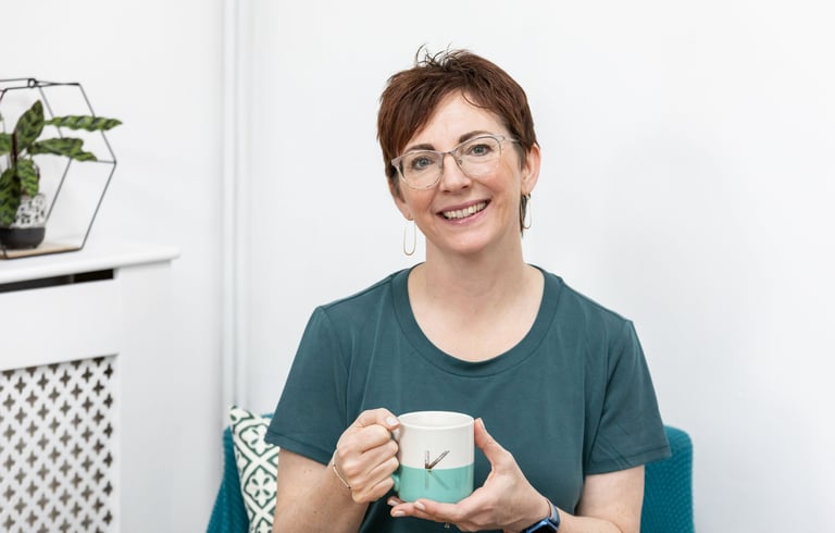 Kelly smiling holding a mug and wearing a green t shirt. 