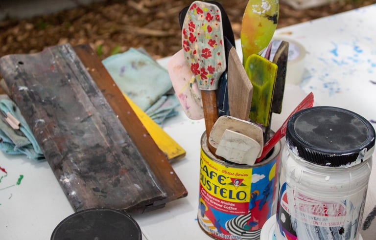 Printmaking materials resting on a table, including spatulas, ink, and a squeegee.