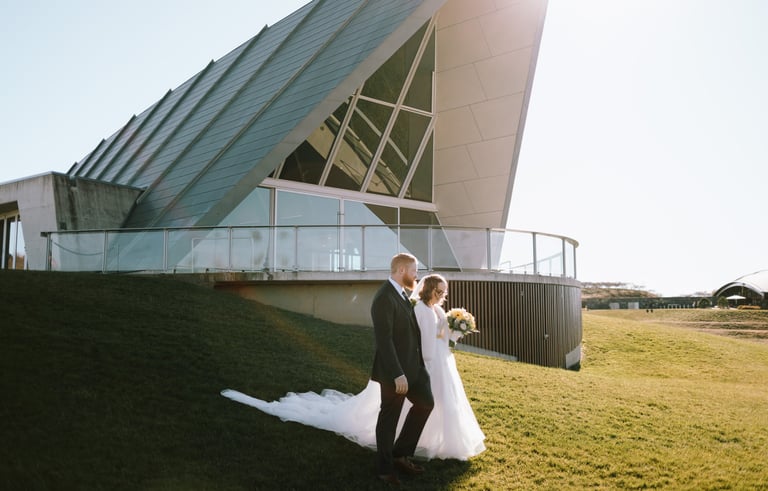 Bride and groom walking down a hill, wedding venue in the background, Canberra wedding photographer
