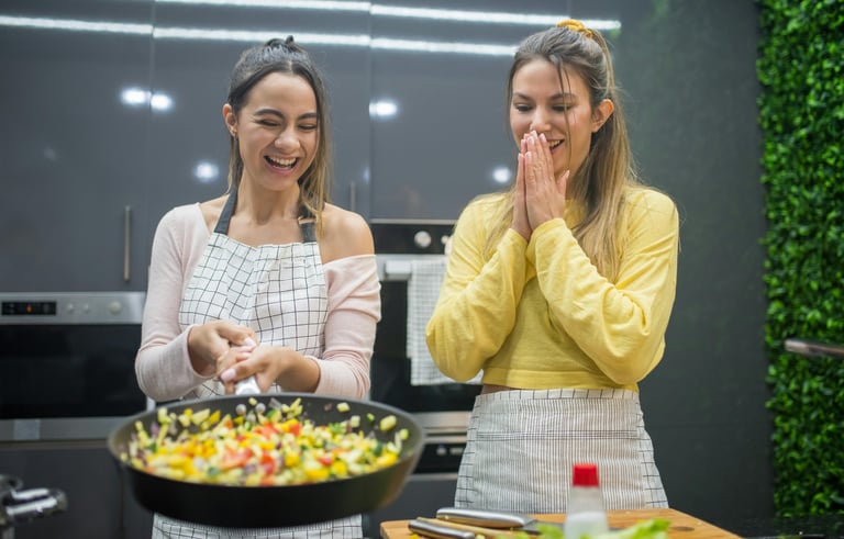 Two women making a meal in a pan and smiling