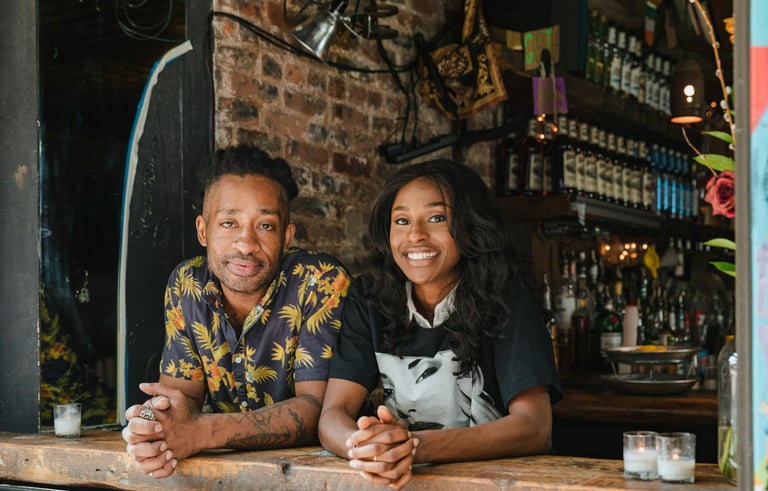Two restaurant owners smiling in the window of their business