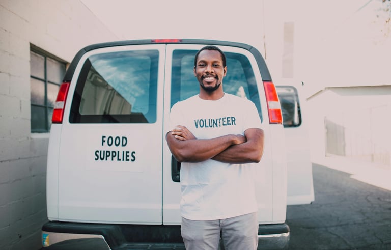 A male volunteer smiling and standing in front of a van with food donations