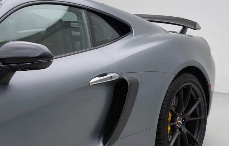 A luxury European sports car in a modern, clean garage environment, showing a flawless application of a satin metallic gray vinyl wrap. The lighting highlights the curves of the vehicle and the premium texture of the foil.