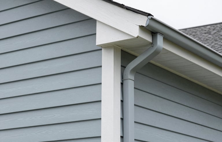 Close-up architectural photography of light blue-gray vinyl siding and seamless gutters on a North American home. Sharp focus, clean lines, professional craftsmanship with muted gray tones.