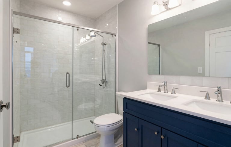 Modern master bathroom renovation in a North American / Hispanic residence. Features a walk-in glass shower, subway tiles, and a double vanity with indigo blue accents. Professional lighting highlighting clean grout lines and quality fixtures.