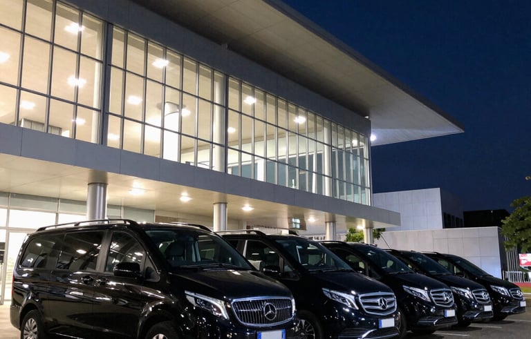A line of identical black luxury vans and sedans parked in front of a modern South American convention center at night, sophisticated urban lighting in navy and steel blue tones.