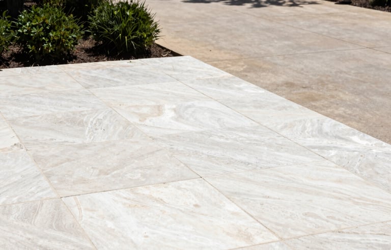 A bright, high-contrast photograph of a limestone patio and stone driveway in Austin, Texas, being meticulously cleaned. The stone looks refreshed and bright. Surrounding the stone are dark green bushes and elegant landscape lighting. The aesthetic is clean and modern.