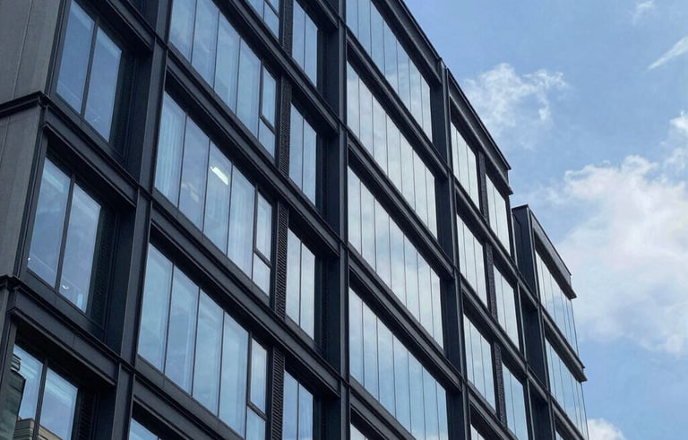 A high-end architectural photograph of a sleek, contemporary multi-story building exterior in a North American urban environment, featuring clean glass and dark navy metal accents under a bright blue sky.