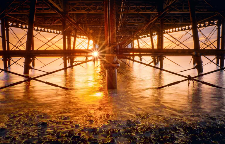 the sunrising through the structure under the pier. sun reflecting on the sea