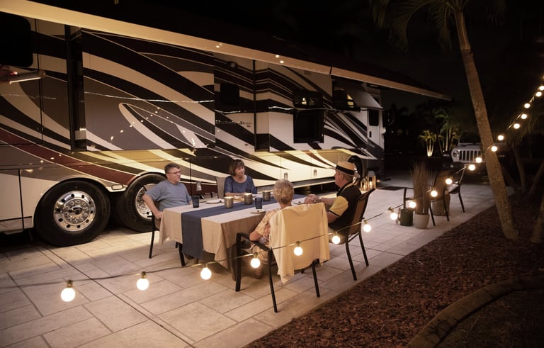 Two senior couples enjoying an outdoor dinner at night beside a luxury Class A RV motorhome.