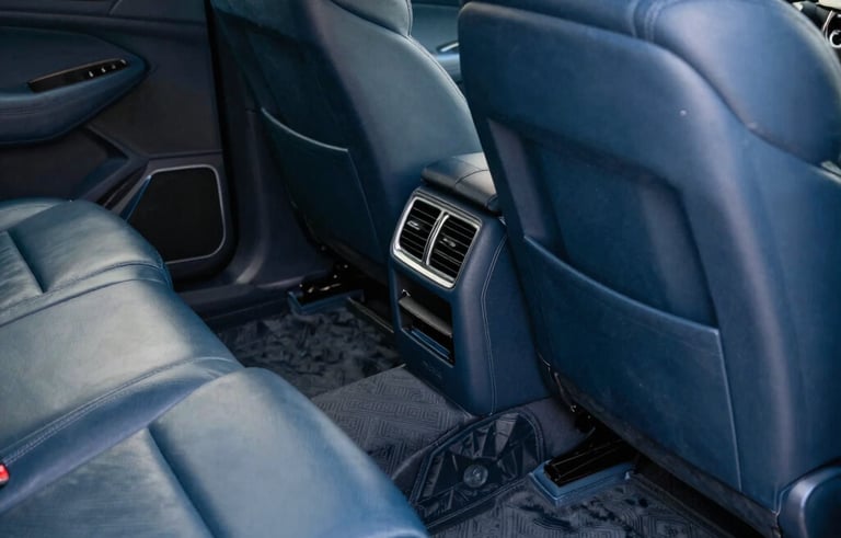 Detailed interior of a luxury vehicle in a North American / US garage, focusing on a perfectly vacuumed floor and conditioned leather seats, soft focused lighting, muted blue color palette.