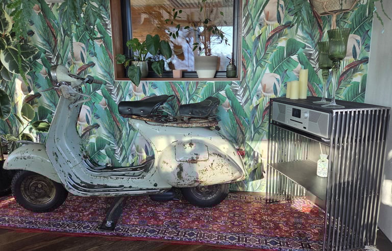 Vintage-Vespa als dekoratives Highlight vor Dschungel-Tapete neben modernem Holz-Sideboard.