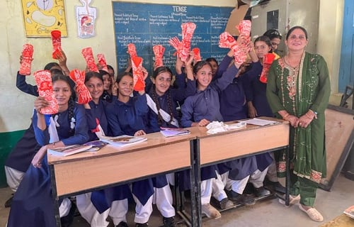 About 12 girls in classroom holding up napkin packs.