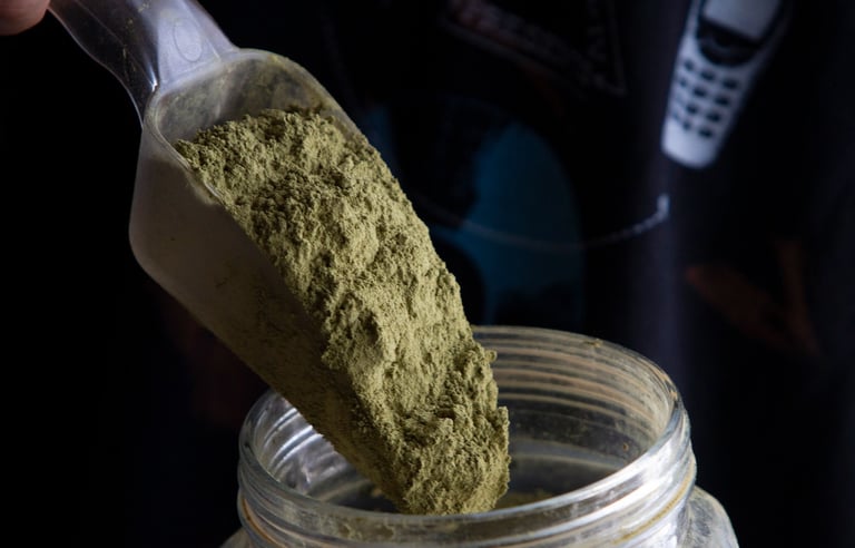 A plastic scoop pouring organic green kratom powder into a glass storage jar.