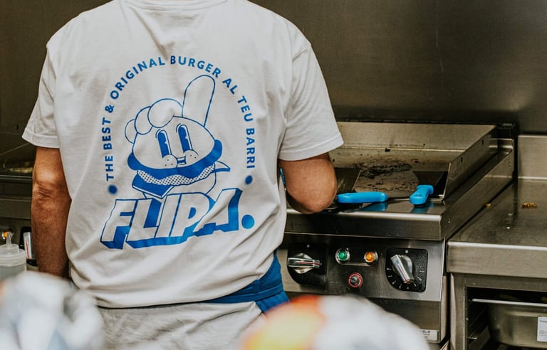 Cuiner de Flipa a la cuina amb samarreta de la marca mentre prepara burgers a la planxa