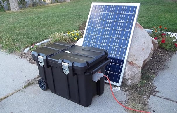 Portable solar power generator kit with a black battery case and solar panel set up outdoors.